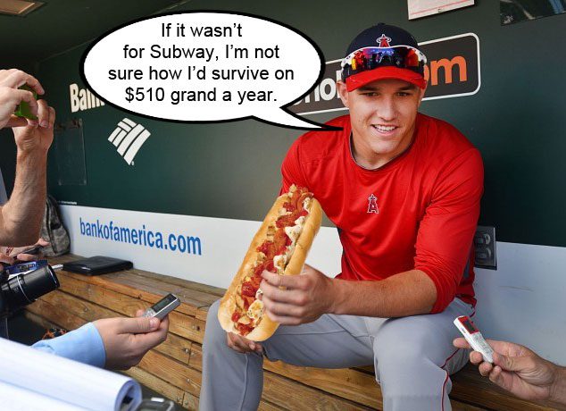 Mike Trout holds a Subway sub (composite image) while talking to reporters in the dugout.