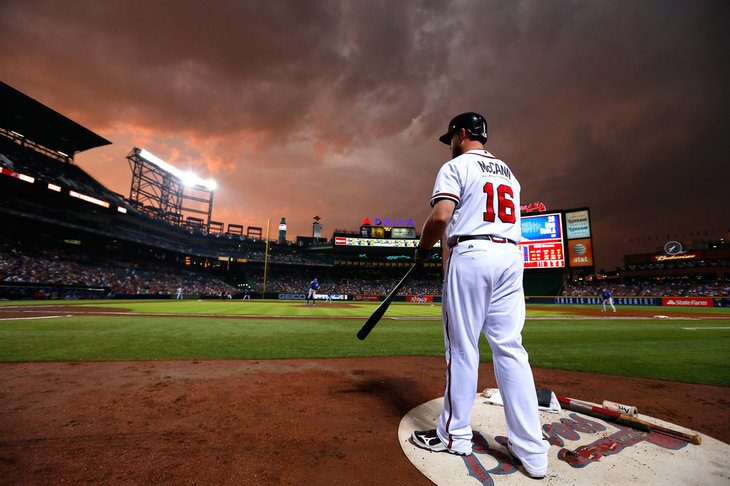 Brian McCann stands in the on-deck circl with a vibrant sunset sky in the background.