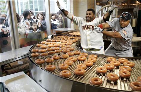 Composite image of Pablo Sandoval with arms raised and Carlos Lee diving to try and beat him to the Krispy Kreme conveyor of donuts.