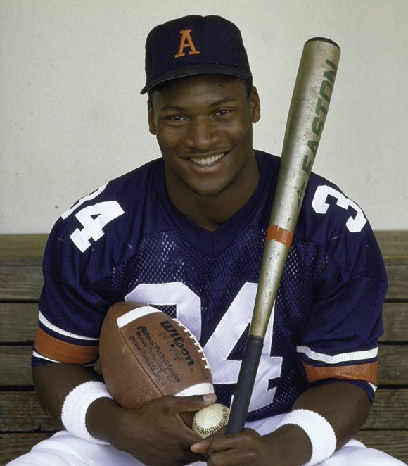 Bo Jackson holding a football, baseball and baseball bat during his days at Auburn.